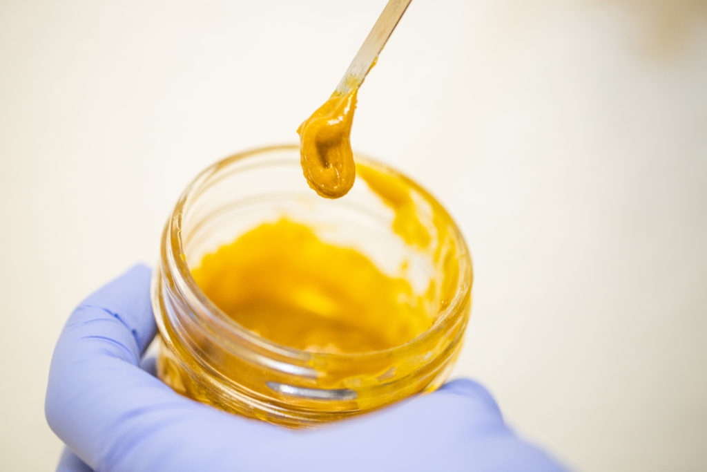A hand holding a jar of Cannabis concentrates